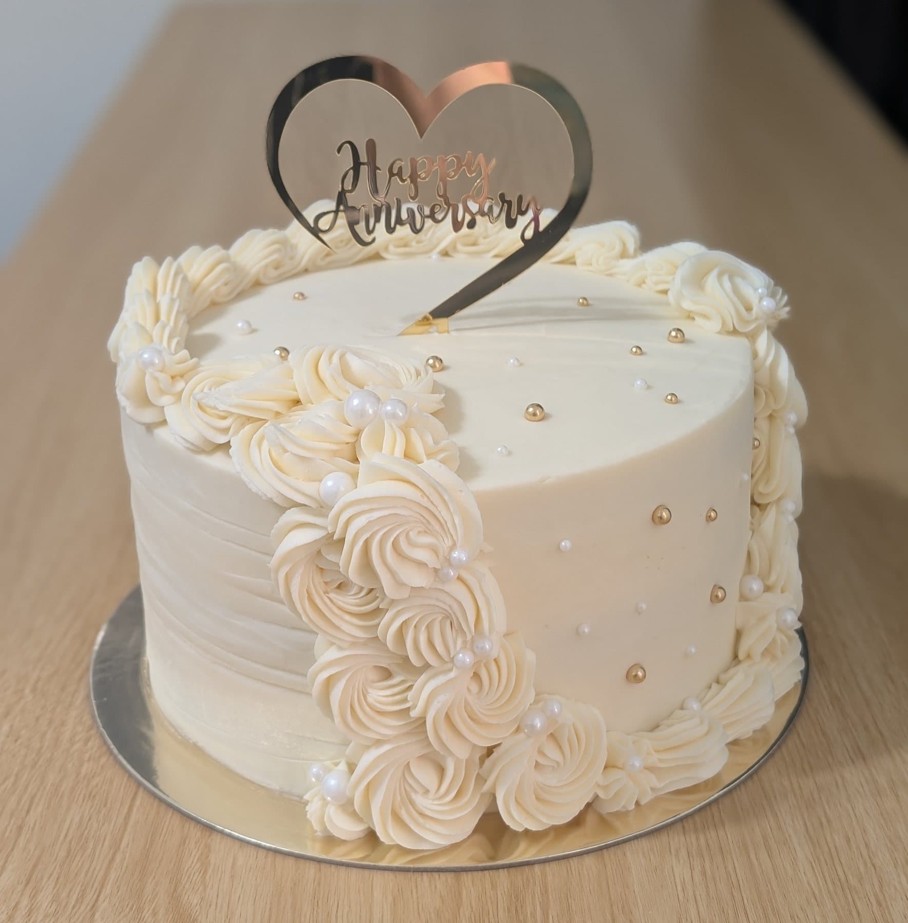 A single-tier ivory cake with a cascade of piped rosettes, pearl accents and a gold anniversary topper