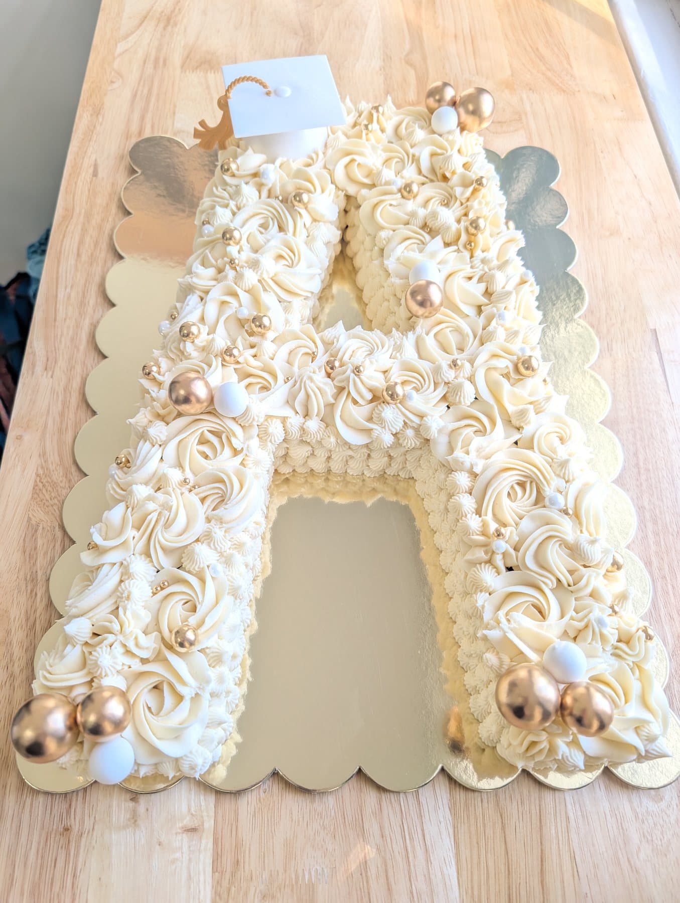 A cake shaped as the letter A, covered in ivory piped rosettes with gold pearl accents, on a scalloped gold board