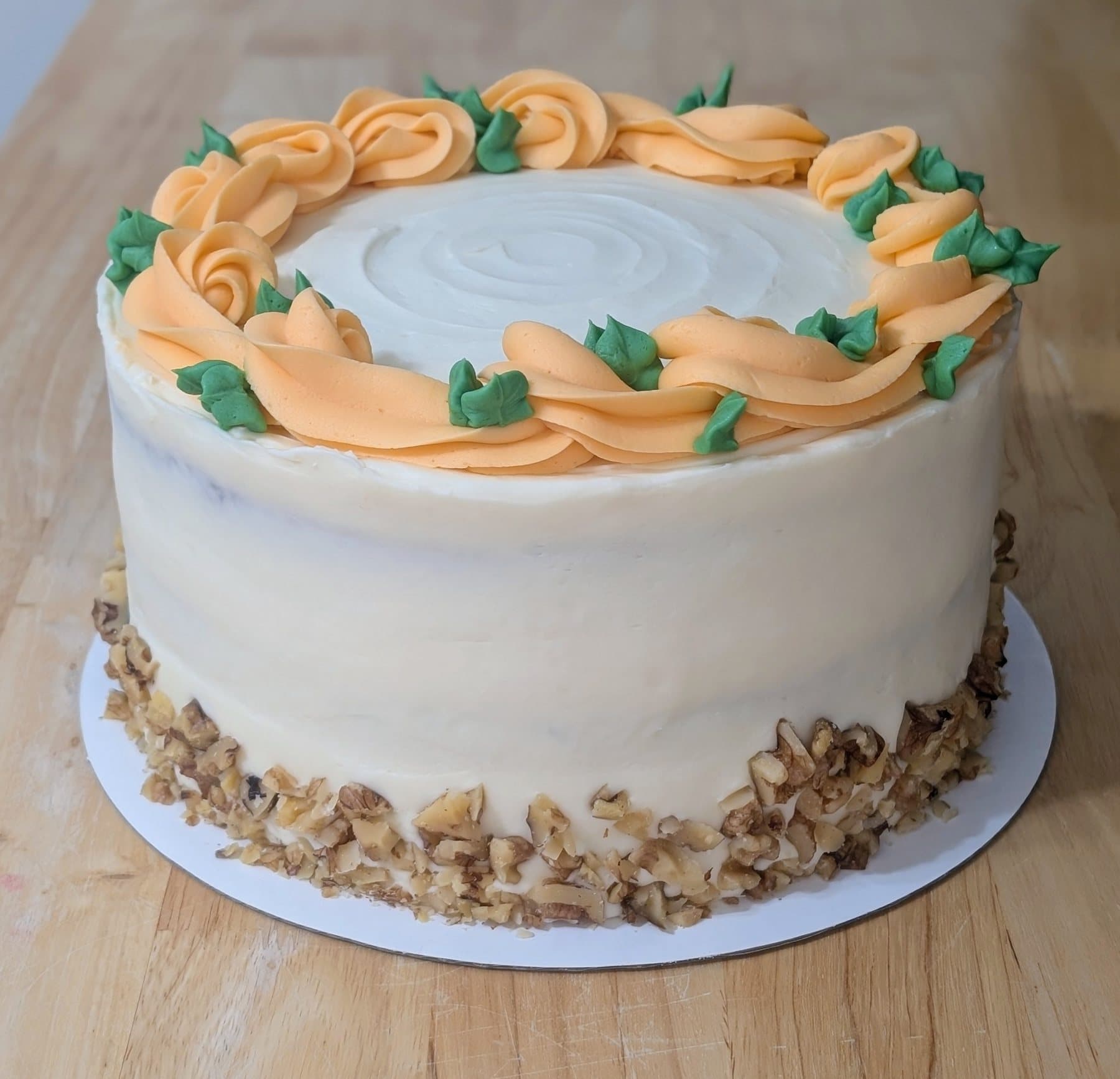 A round cake with a pale top framed by orange and green piped leaves above a textured buttercream base