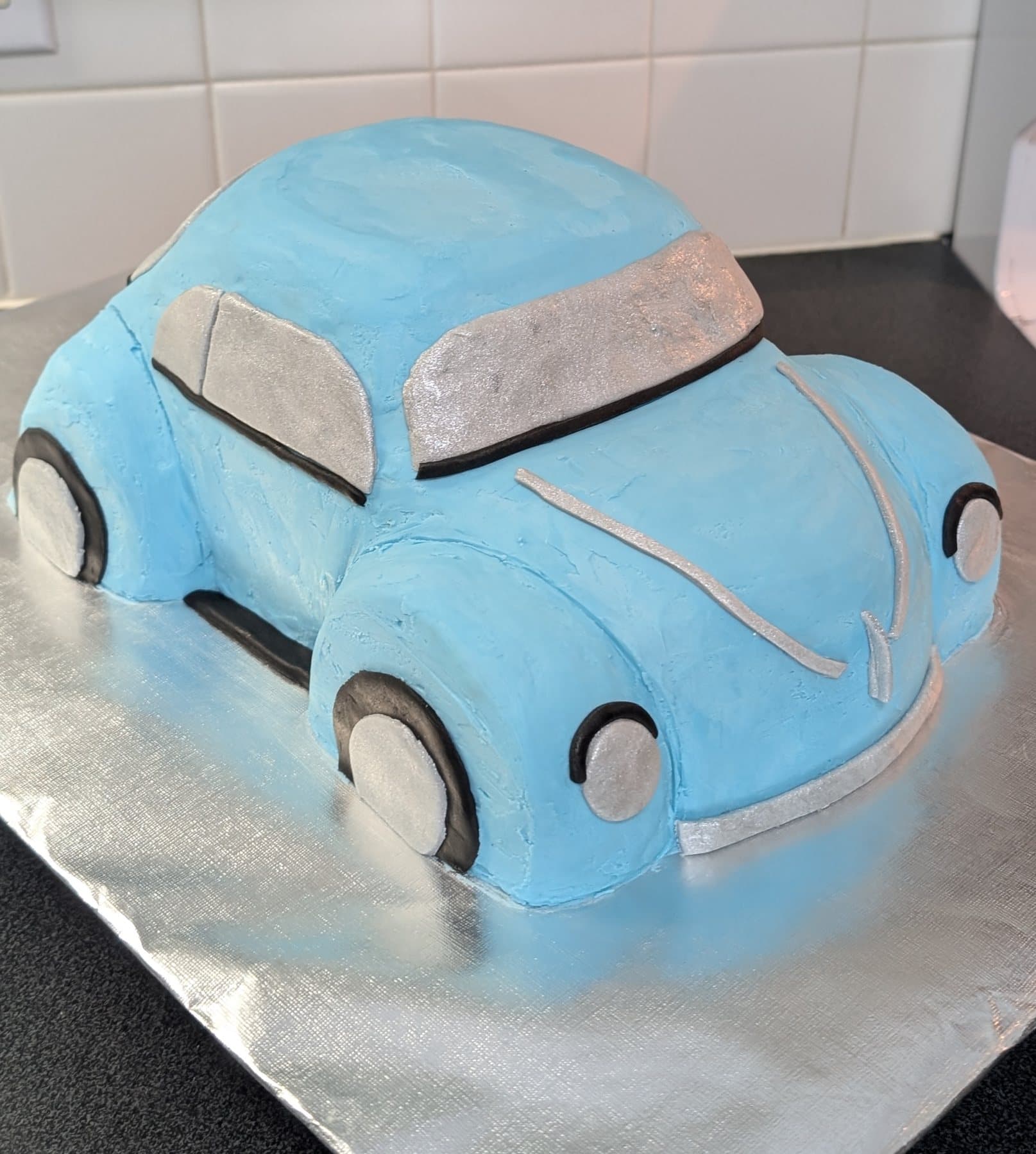 A cake sculpted and finished as a pale blue vintage car, with silver piped detailing for the windows, bumpers and wheels