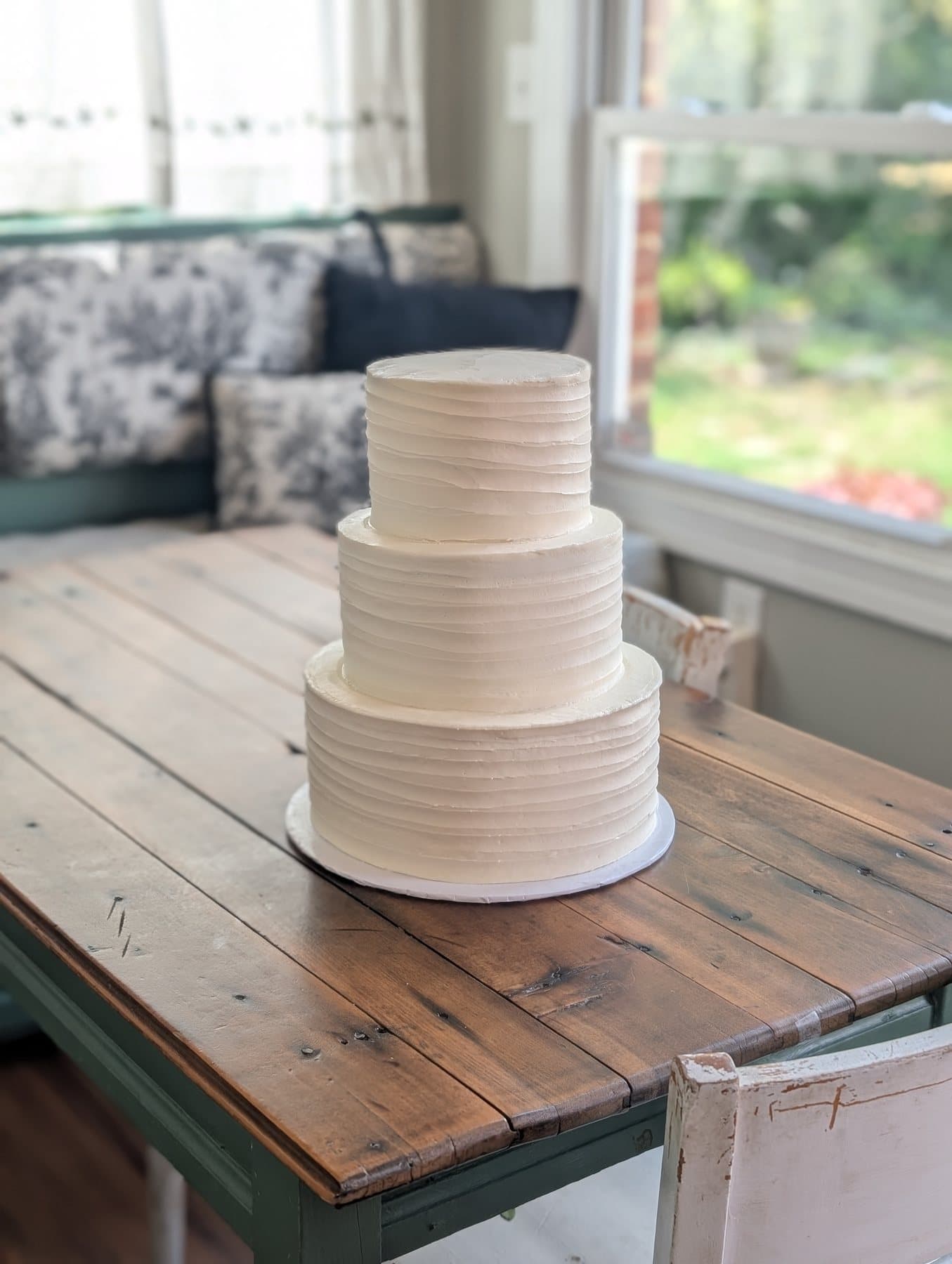 A two-tier ivory wedding cake in horizontally combed buttercream, on a wooden table in window light